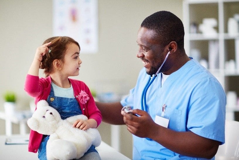 A doctor is holding a teddy bear and talking to a little girl.