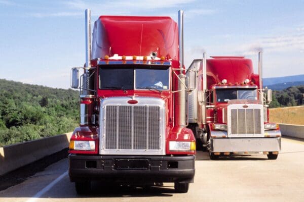 Two red trucks are driving down the road.